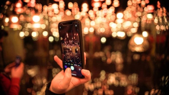 The Mad Dimension : le premier musée 100% instagrammable au cœur de Paris Une personne prenant des photos avec son smartphone avec des bokeh en arrière-plan.